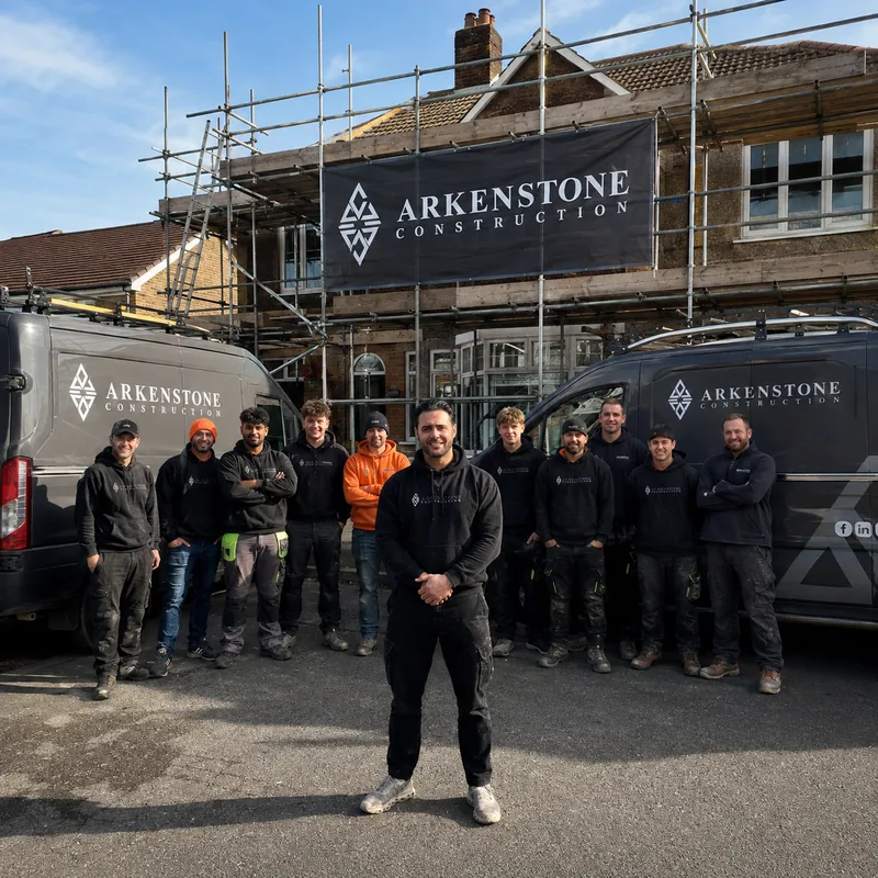 Charles Stevens, owner of Arkenstone Construction, front and centre with the Arkenstone team, two liveried vans and a scaffolded roofing job behind them